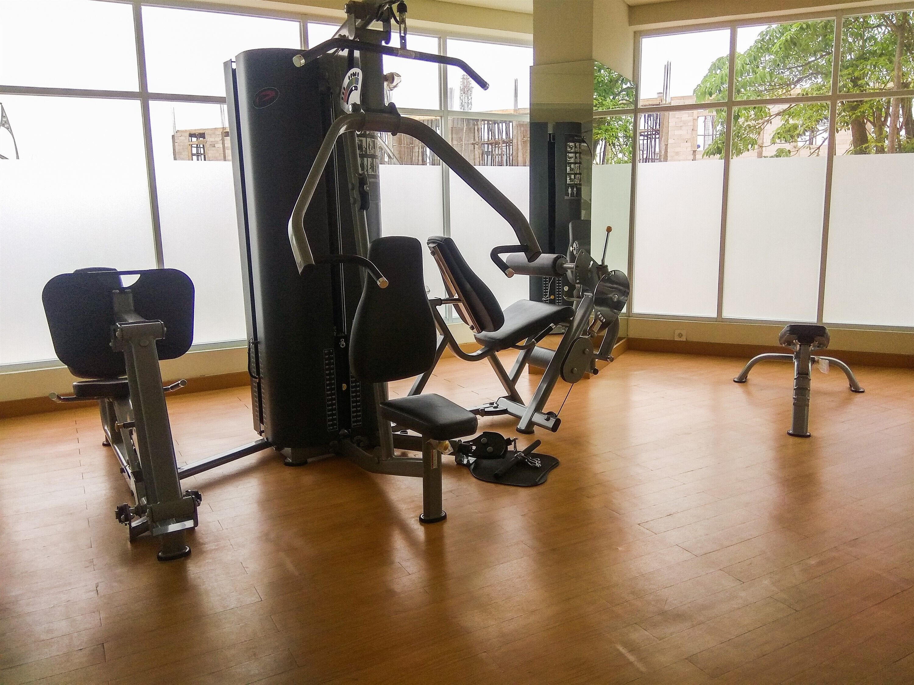 A gym with various exercise machines, large windows, and a wooden floor.