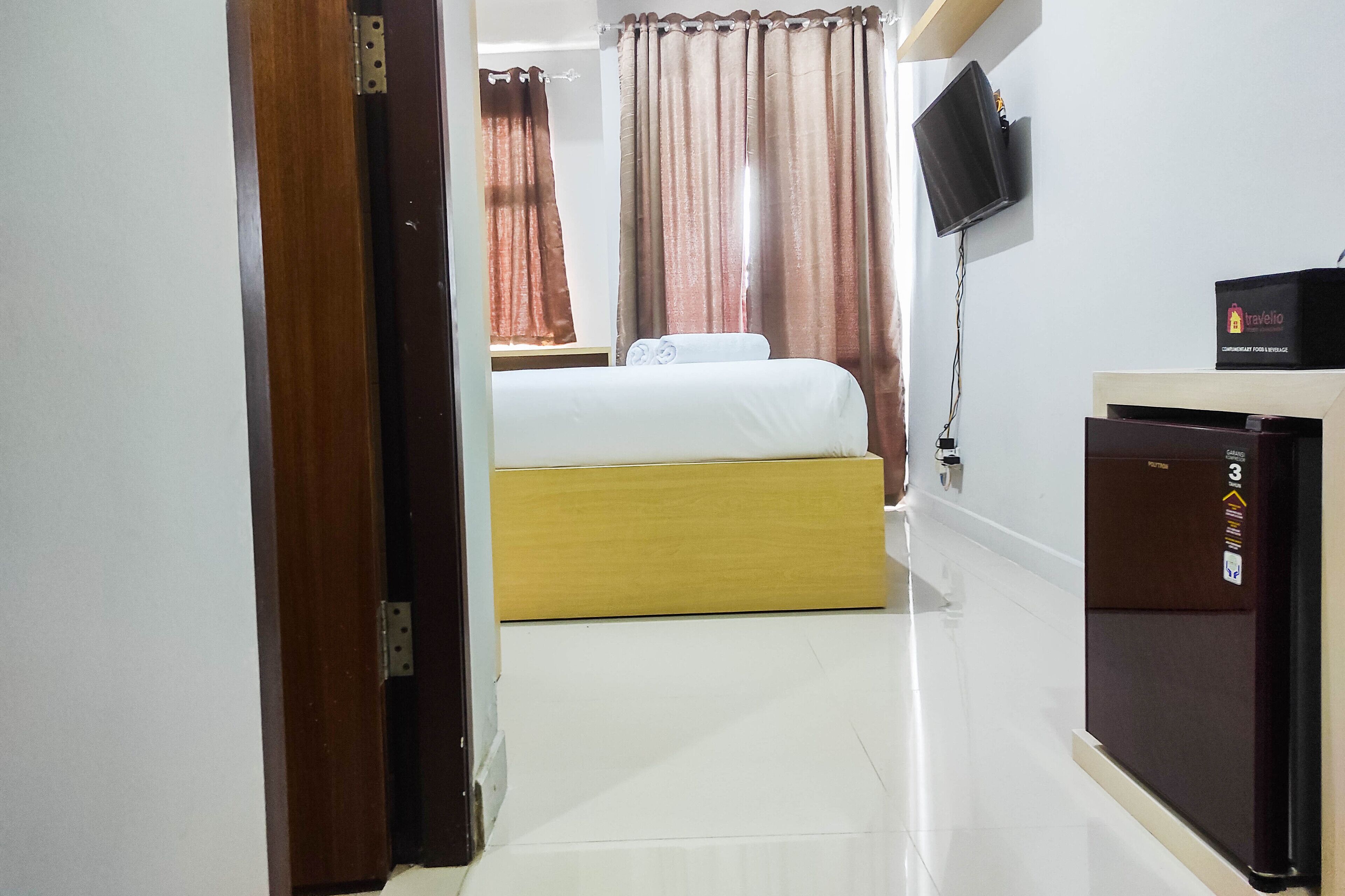 A hotel room with a bed, a television mounted on the wall, and a refrigerator.