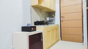 Eine kleine Küchenzeile mit Kühlschrank, Mikrowelle, Kaffeemaschine und einer Reisetasche auf der Arbeitsplatte.