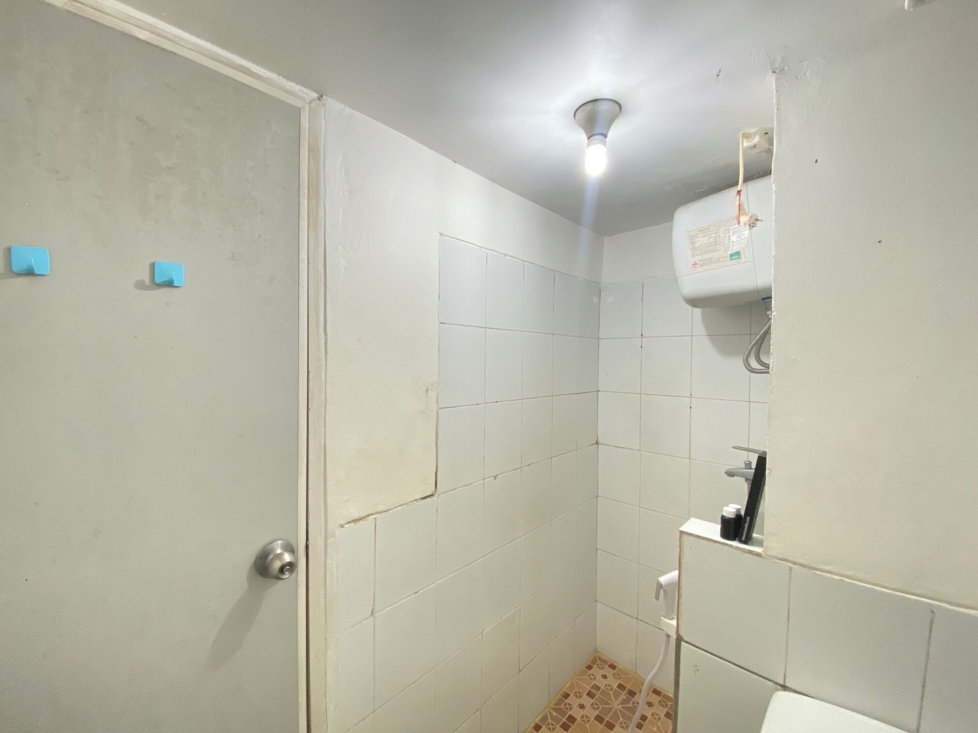 A bathroom with white tiles, a shower area, a toilet, and a ceiling light.