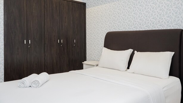 A bedroom with a large dark wooden wardrobe, a white bed with two pillows, and a white nightstand. - Comfortable And Nice 1Br At Branz Bsd Apartment (Pagedangan)