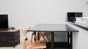 A modern kitchen with a black countertop, a microwave, and a coffee machine. There is a wooden table with four chairs. - Comfortable And Nice 1Br At Branz Bsd Apartment (Pagedangan)