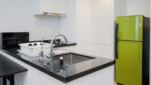 A modern kitchen with a black countertop, stainless steel sink, and a green refrigerator. - Comfortable And Nice 1Br At Branz Bsd Apartment (Pagedangan)