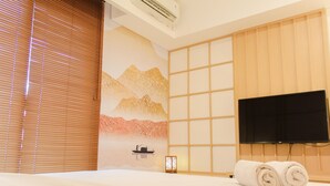 A hotel room with a bed, a flat-screen TV, a wall-mounted air conditioner, and a window with blinds. - Japanese Cozy Style Studio At Bintaro Embarcadero Apartment (South Tangerang)