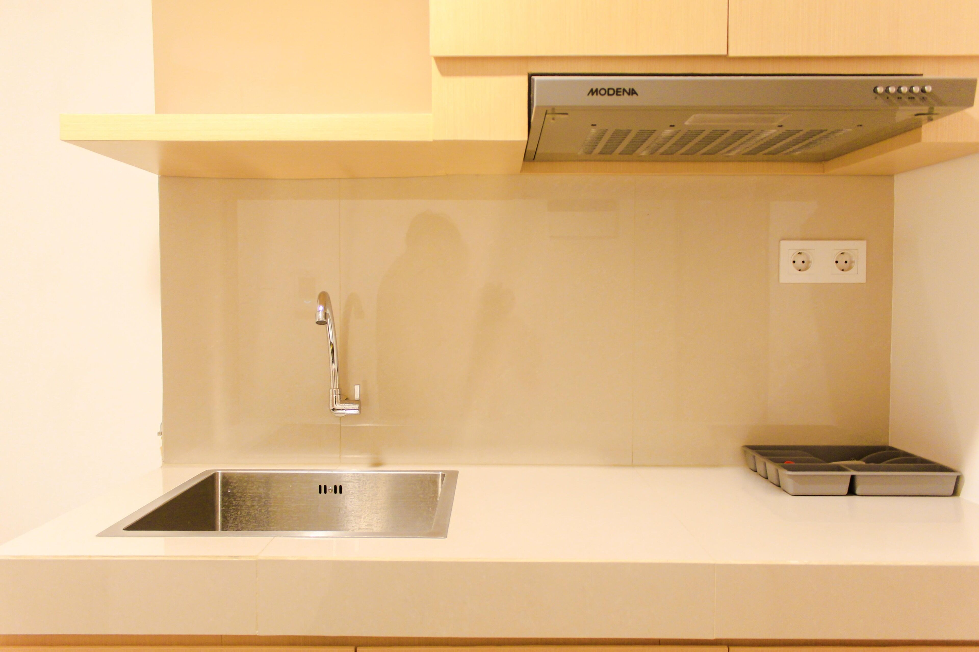 Una cocina moderna con un lavamanos de acero inoxidable, una campana extractora integrada y una toma de corriente doble.