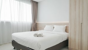 A neatly made bed with white linens and two rolled towels, a wooden headboard, and a wardrobe with a light wood finish. - Comfortable And High Floor 1Br Paddington Heights Apartment (Tangerang)