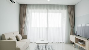 A modern living room with a sofa, a small table, a TV, and a large window with curtains. - Comfortable And High Floor 1Br Paddington Heights Apartment (Tangerang)