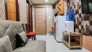 A living room with a sofa, a small table, and a TV mounted on the wall. - Luxurious 2Br At Vida View Makassar Apartment (Makassar)