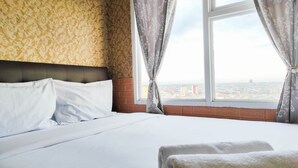 A hotel room with a large bed, white bedding, a patterned wallpaper, and a view of the city through a window with curtains. - Luxurious 2Br At Vida View Makassar Apartment (Makassar)