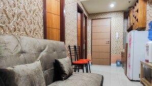 A living room with a sofa, a small table, and a red chair. There is a wooden cabinet and a white refrigerator in the background. - Luxurious 2Br At Vida View Makassar Apartment (Makassar)