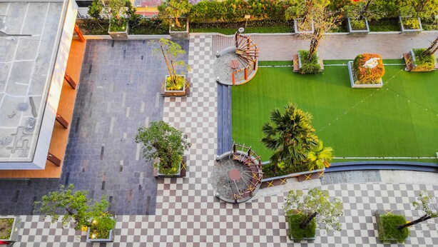 An aerial view of a courtyard with a checkered floor, a spiral staircase, and surrounding greenery. - Luxurious 2Br At Vida View Makassar Apartment (Makassar)