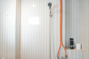 A shower with a handheld showerhead and a wall-mounted faucet, a towel rack, and a shelf with toiletries. - Luxury 2Br At Cinere Resort Apartment (Depok)