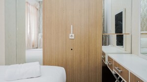 A hotel room with a wooden wardrobe, a white bed, a bathroom with a mirror, and a white towel on the bed. - Comfort 2Br At Serpong Greenview Apartment (South Tangerang)