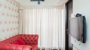 A room with a red leather sofa, a flat-screen TV mounted on the wall, and a window with white curtains. - Comfort 2Br At Serpong Greenview Apartment (South Tangerang)