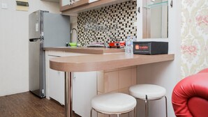 A compact kitchen with a refrigerator, a microwave, a sink, and a small countertop. There are two stools and a box labeled 'travelio'. - Comfort 2Br At Serpong Greenview Apartment (South Tangerang)