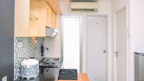 A compact kitchen with a stove, sink, and a microwave. There is a small refrigerator and a cabinet above the sink. - Alluring 2Br At Bassura City Apartment Near Mall (Jakarta)
