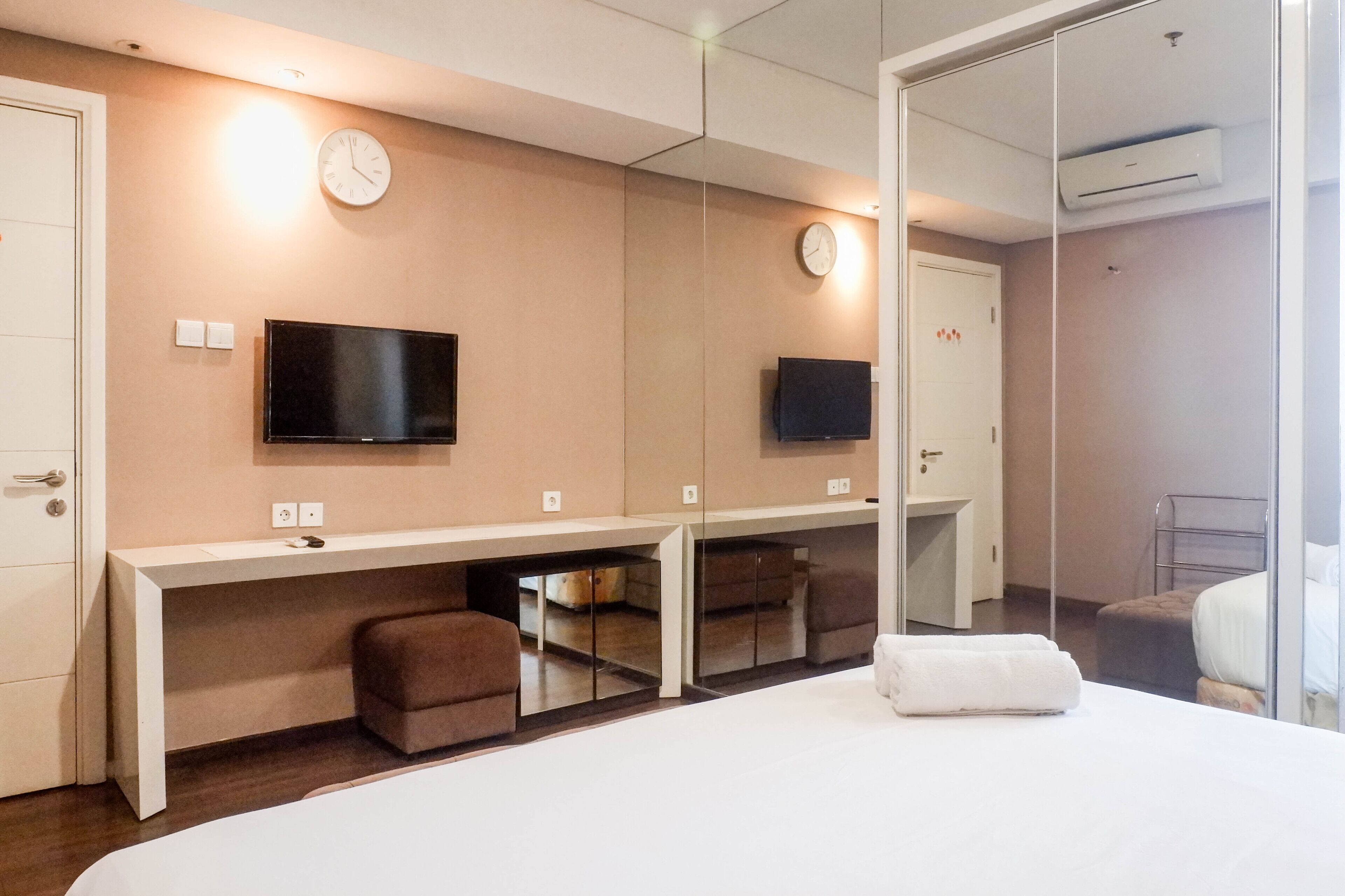 Une chambre d’hôtel avec un grand lit, un bureau doté d’un téléviseur à écran plat, un miroir et une horloge murale.
