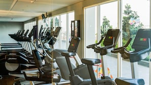 Ein Fitnessraum mit mehreren Laufbändern und Crosstrainern, die in Reihen angeordnet sind, mit großen Fenstern und Blick ins Freie.