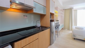 Eine moderne Küche mit eingebautem Herd, Spüle und Kühlschrank. Es gibt eine kleine Essecke mit Tisch und Stühlen. Im Hintergrund ist ein Bett zu sehen.