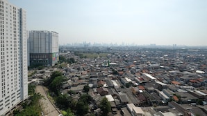 A high-rise building with multiple floors and a dense urban area with numerous smaller buildings in the background. - Comfort Living Bassura City Studio Apartment Near Mall (Jakarta)