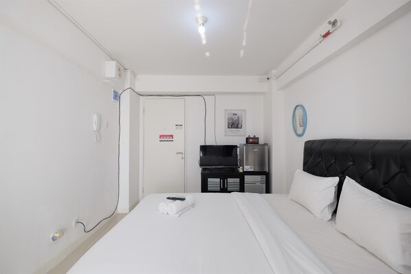 Habitación de hotel con cama, televisión, minibar y puerta con letrero rojo.