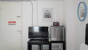 A hotel room with a closed door, a flat-screen TV on a black cabinet, a GE refrigerator, and a framed cityscape photo on the wall. - Comfort Living Bassura City Studio Apartment Near Mall (Jakarta)