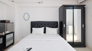 A hotel room with a bed, a wardrobe, a small desk with a phone, and a mirror on the wall. - Comfort Living Bassura City Studio Apartment Near Mall (Jakarta)