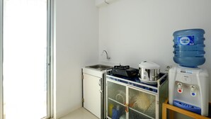 A compact kitchen with a sink, a small refrigerator, a water dispenser, and a large water bottle. - Comfort Living Bassura City Studio Apartment Near Mall (Jakarta)