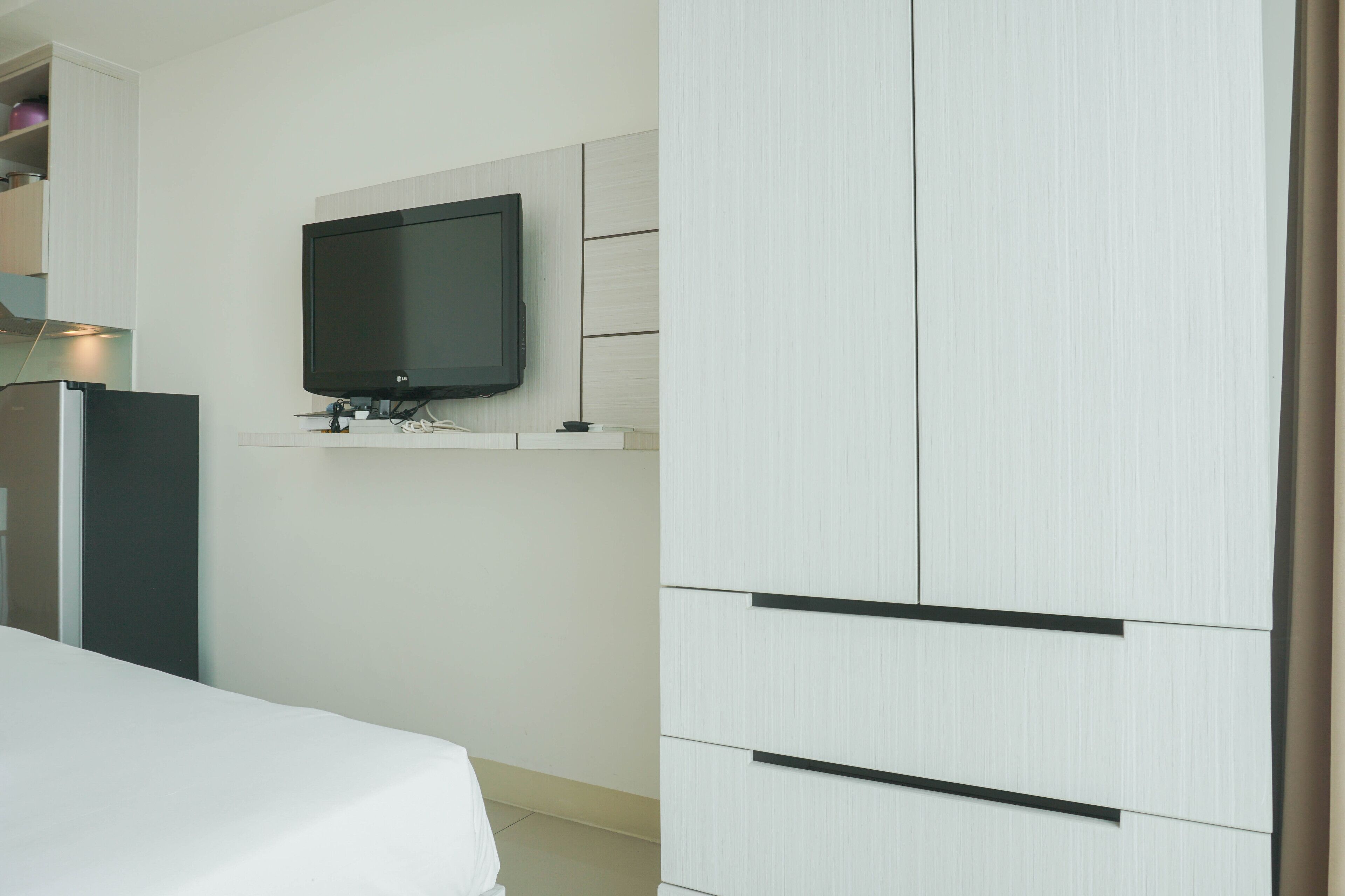 A modern hotel room with a bed, a flat-screen TV mounted on the wall, and a wardrobe with multiple compartments.