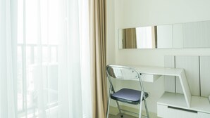 A modern room with a clear view of the outside through sheer curtains, a foldable chair, a white desk, and a mirror on the wall. - Comfortable Studio Room At Tree Park Bsd Apartment (South Tangerang)