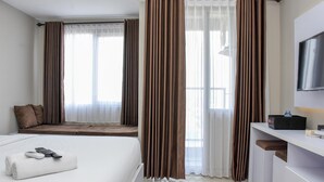 Quarto de hotel com cama, escrivaninha, televisão e janela com cortinas.