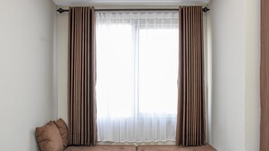 Um quarto com janela, um sofá marrom e uma cortina branca.
