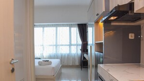 Habitació d'hotel senzilla amb llit, escriptori i cuina americana.