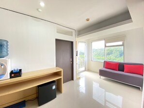 Enjoy a bright and inviting room with a large window offering a view of lush greenery, a comfortable sofa, and a flat-screen TV.