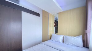 A hotel room with a large bed, a wooden wardrobe, and a mirror. - Quite 2Br Apartment Ac In Living Room At The Jarrdin Cihampelas (Bandung)