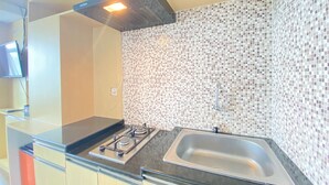 A modern kitchen with a gas stove, stainless steel sink, and a tiled backsplash. - Quite 2Br Apartment Ac In Living Room At The Jarrdin Cihampelas (Bandung)