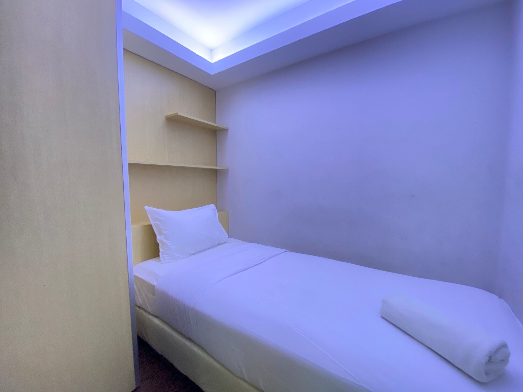 Une petite chambre avec un lit simple, une lucarne, une étagère près du lit et un lit parfaitement fait.