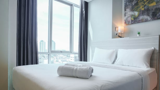 A hotel room with a large bed, a view of the city through a window, and a modern abstract painting on the wall. - Great Choice Deluxe Studio Apartment At Capitol Park Residence (Jakarta)