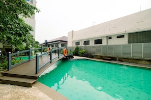 A swimming pool with a wooden deck and a bridge, surrounded by greenery and buildings. - Great Choice Deluxe Studio Apartment At Capitol Park Residence (Jakarta)