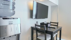A water dispenser, a flat-screen TV, and a table with chairs in a room. - Great Choice Deluxe Studio Apartment At Capitol Park Residence (Jakarta)