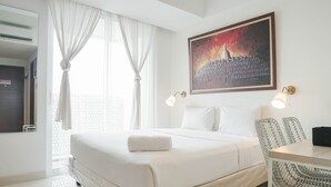 A hotel room with a large bed, a dining table with chairs, a painting on the wall, and a window with curtains. - Minimalist Studio Room With City View At West Vista Apartment (Jakarta)