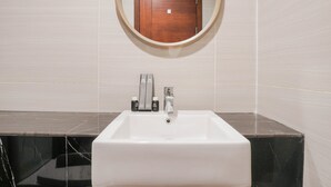 A bathroom with a white sink, two faucets, and a mirror above it. - Minimalist Studio Room With City View At West Vista Apartment (Jakarta)