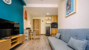 A modern living room with a grey sofa, wooden entertainment unit, and a kitchen area in the background. - Simply 1Br Apartment At Pejaten Park Residence (Jakarta)