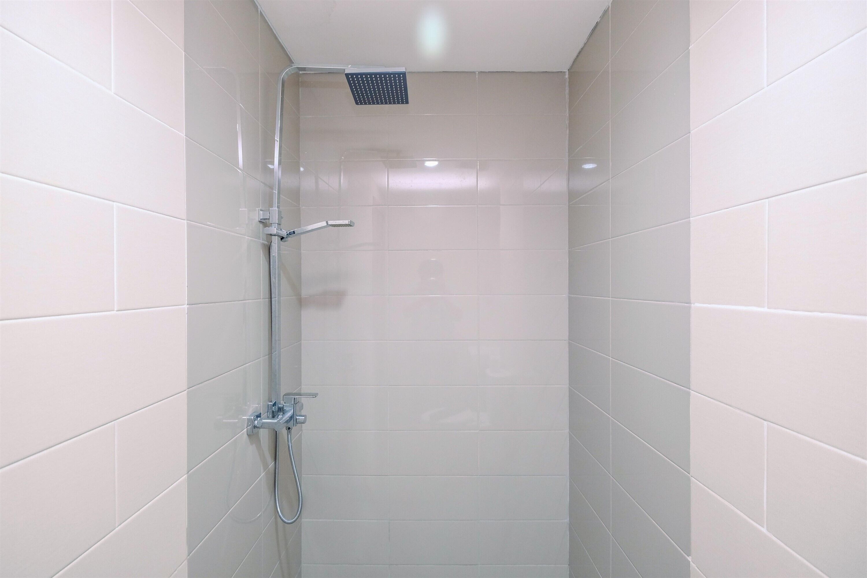 A small, tiled shower stall with a handheld showerhead and a fixed showerhead.