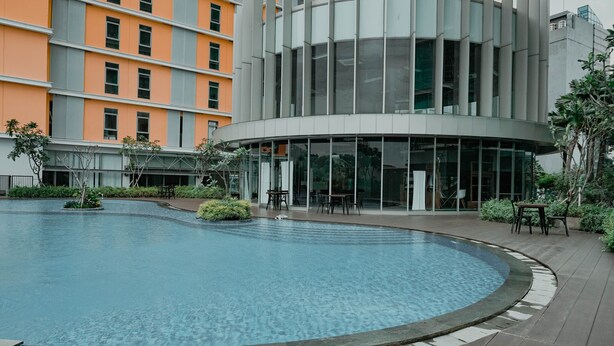 A modern building with a circular pool, outdoor seating, and a glass facade. - Simply 1Br Apartment At Pejaten Park Residence (Jakarta)