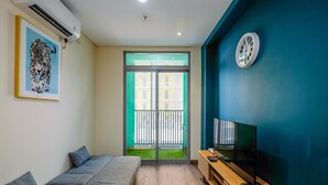 A modern room with a grey sofa, a wooden TV stand, a framed picture of a leopard, and a large window with a view of a building and a balcony. - Simply 1Br Apartment At Pejaten Park Residence (Jakarta)