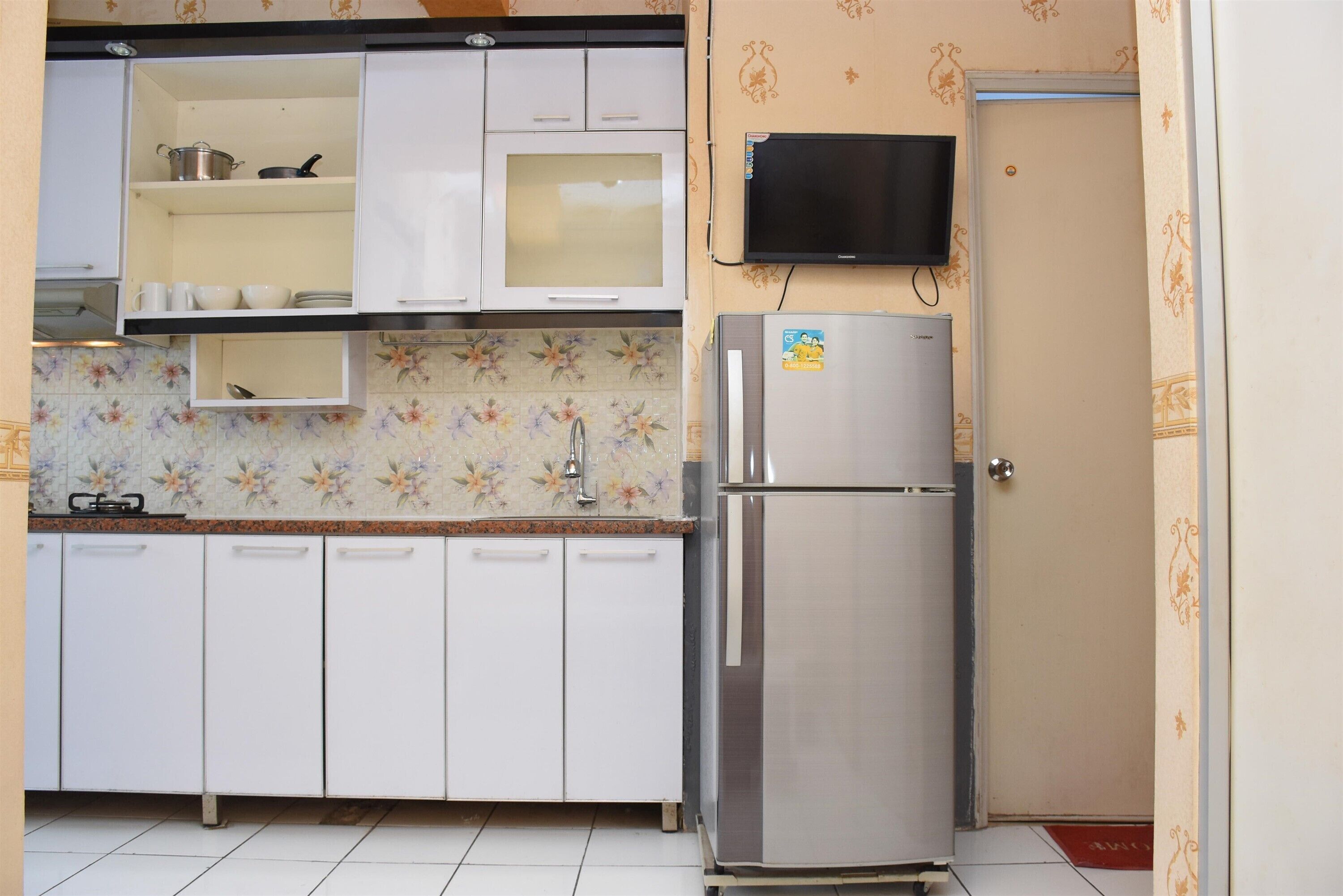 Cozinha compacta com armários brancos, geladeira de aço inoxidável, micro-ondas e painel de azulejos.