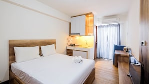 Hotellihuone, jossa on puinen sänky, pieni keittokomero, työpöytä ja kylpyhuone, jossa on suihkuverho.