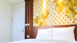 Ett hotellrum med en stoppad sänggavel, vita sängkläder och en garderob i trä.