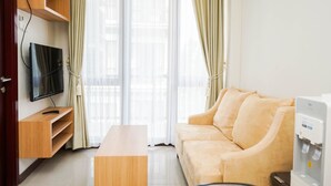 Un salon moderne comprenant un canapé, une table basse, un téléviseur fixé sur une étagère en bois et un distributeur d’eau.